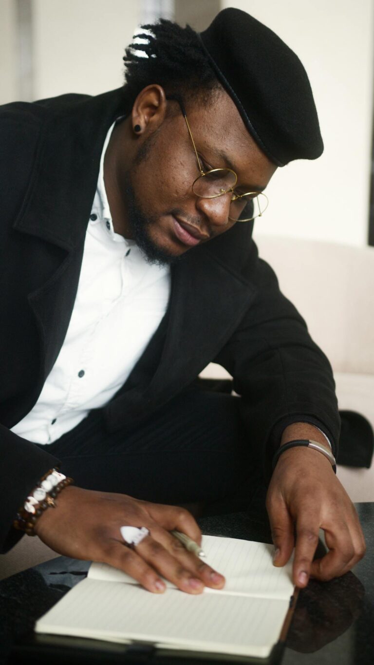 A Man in Black Long Sleeves Writing on a Notebook